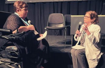 Rollespil på scene. En kvinde i kørestol spiller patient overfor en kvinde i kittel, der spiller læge.