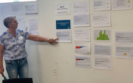 Bente Nikolajsen fra Plejeboligerne Center Vest i Holstebro står og peger på et whiteboard med opsatte papirer og skemaer.