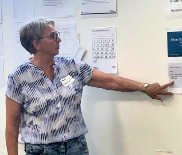 Bente Nikolajsen fra Plejeboligerne Center Vest i Holstebro står og peger på et whiteboard med opsatte papirer og skemaer.