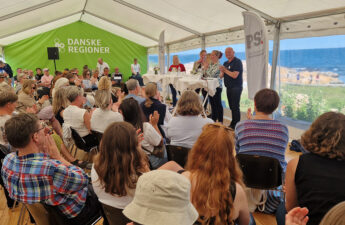 Et fyldt telt med ca. 100 tilskuere. De kigger op mod paneldeltagerne, og i baggrunden ses havet.