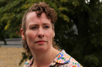 Portræt af Annelene Højvang Larsen taget udendørs. Hun har kort, krøllet hår og blomstret skjorte og ser forbi kameraet.