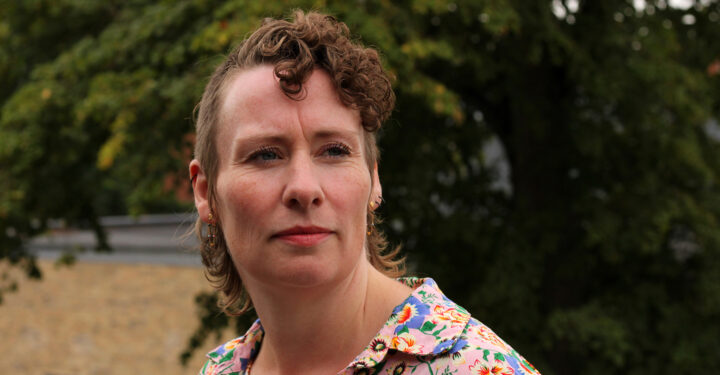 Portræt af Annelene Højvang Larsen taget udendørs. Hun har kort, krøllet hår og blomstret skjorte og ser forbi kameraet.