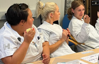 Tre kvinder i hvide sygeplejerskeuniformer sidder ved et bord. Der ligger papirer foran dem, og de ser ud til at være i samtale.
