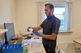 En mand kigger på et pilleglas. Han står alene i et medicinrum og foran er pilleæsker og en kasse med medicin, som han skal dispensere.
