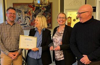 Fire mennesker står med et diplom og en pris. De ser glade ud.