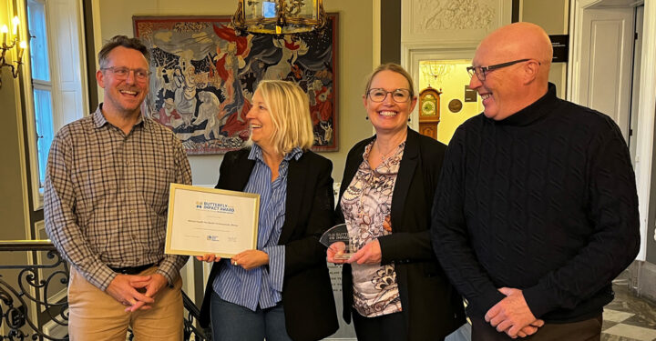 Fire mennesker står med et diplom og en pris. De ser glade ud.