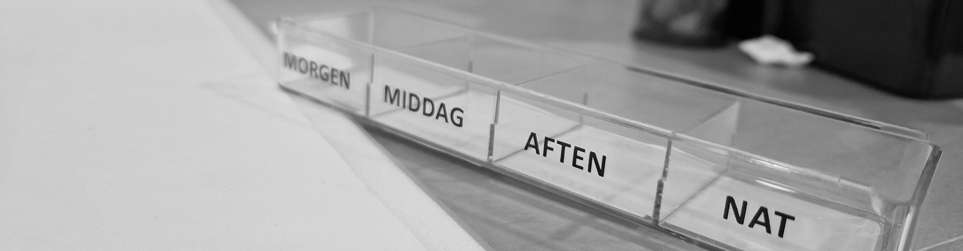 Sort/hvid foto af tom pilleæske med fire felter, hvorpå der står: Morgen, middag, aften og nat.