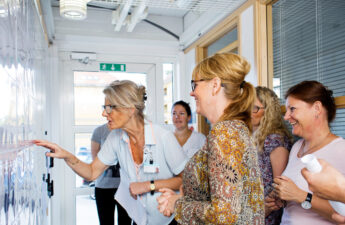 5 kvinder og 1 mand står og smiler, mens de kigger interesseret på en tavle.