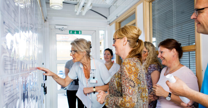 5 kvinder og 1 mand står og smiler, mens de kigger interesseret på en tavle.