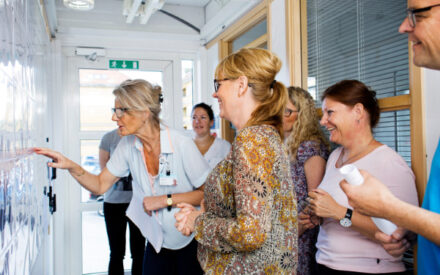 6 kvinder og en mand står og smiler, mens de kigger på en tavle