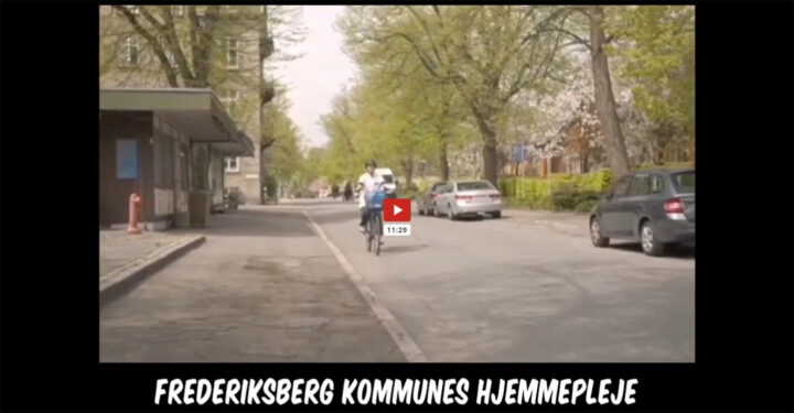 Stillfoto fra video. En ansat fra hjemmeplejen kører på cykel på en øde gade. Foran vises mittal for videoens længde: 11 minutter og 29 sekunder.