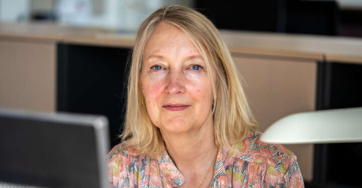 Portræt af Inge Kristensen, der sidder ved en computerskærm, men er vendt mod kameraet.