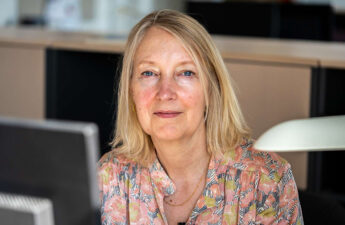 Portræt af Inge Kristensen, der sidder ved en computerskærm, men er vendt mod kameraet.