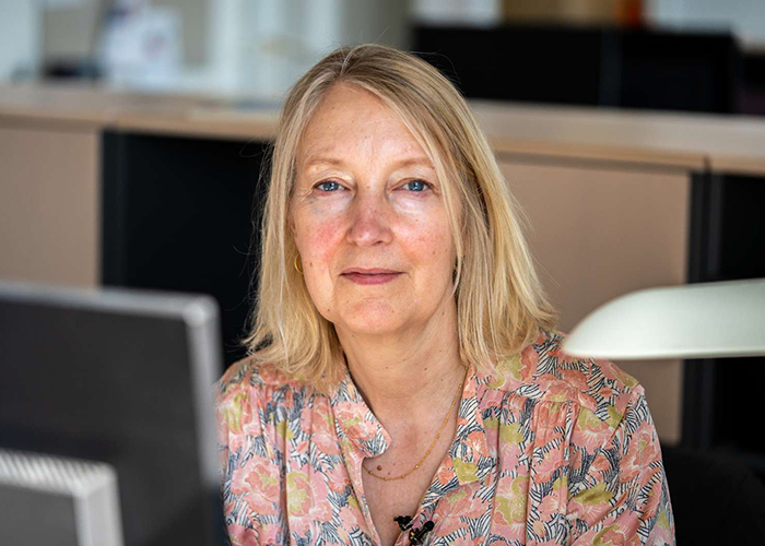 Portræt af Inge Kristensen, der sidder ved en computerskærm, men er vendt mod kameraet.
