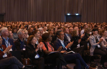 Flere hundrede mennesker sidder og klapper mens de kigger op mod scenen