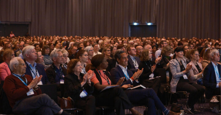 Flere hundrede mennesker sidder og klapper mens de kigger op mod scenen