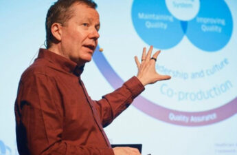 Jason Leitch holder oplæg og peger op mod sin PowerPoint.