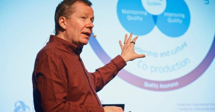 Jason Leitch holder oplæg og peger op mod sin PowerPoint.