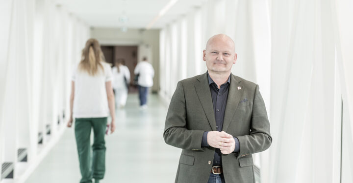 Protrætfoto ved hospitalsgang. I baggrunden går en sundhedsprofesionel med ryggen til.