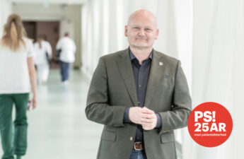 Portrætfoto ved hospitalsgang. I baggrunden går en sundhedsprofesionel med ryggen til.