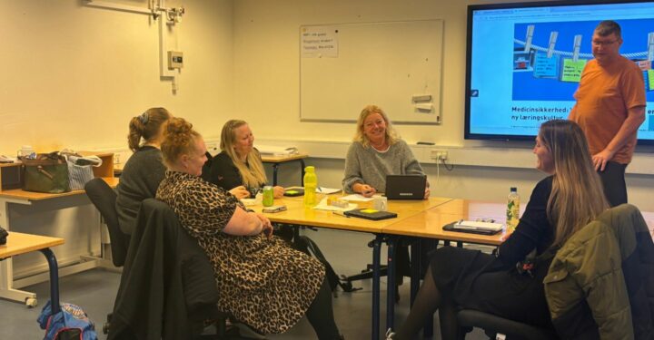 Seks mennesker sidder rundt om et bord og snakker