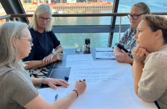 Fire kususdeltagere sidder sammen om et bord og skriver punkter ned på et stort stykke papir