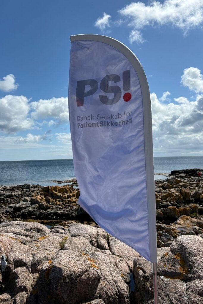 beach-flag med logo for Dansk Selskab for Patientsikkerhed sat fast mellem klipperne på Bornholm